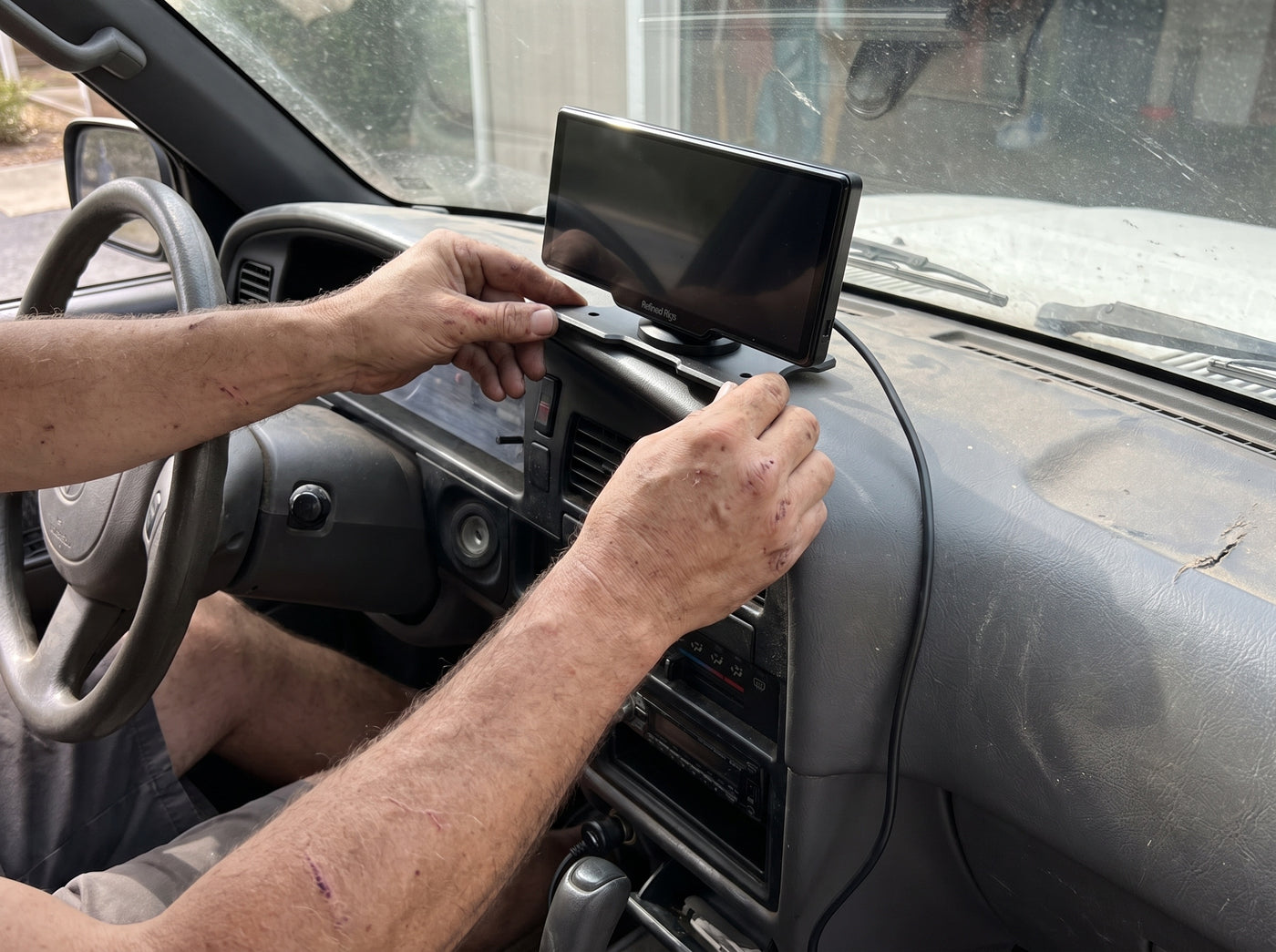 Hands mounting the Evara Display's black plate on the dash of an older Toyota pickup